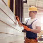 Handsome young man builder installing exterior wood siding